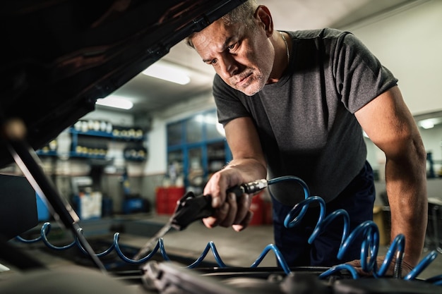 Medio volwassen automonteur die de motor van een auto schoonmaakt met luchtblaaspistool bij reparatiewerkplaats