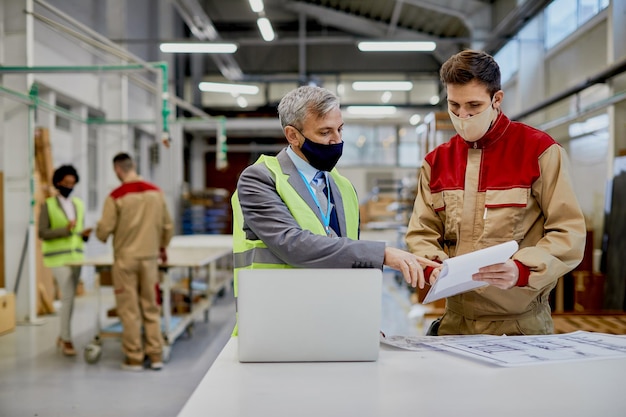 Gratis foto medio volwassen ingenieur en mannelijke werknemer die gezichtsmaskers draagt tijdens het onderzoeken van papierwerk en houtbewerkingsfabriek