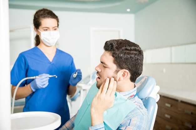 Medio volwassen man die lijdt aan kiespijn tijdens het kijken naar tandarts met gereedschap in de kliniek