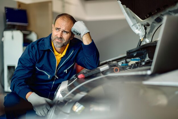 Medio volwassen monteur denken tijdens het repareren van de motor van een auto in een werkplaats