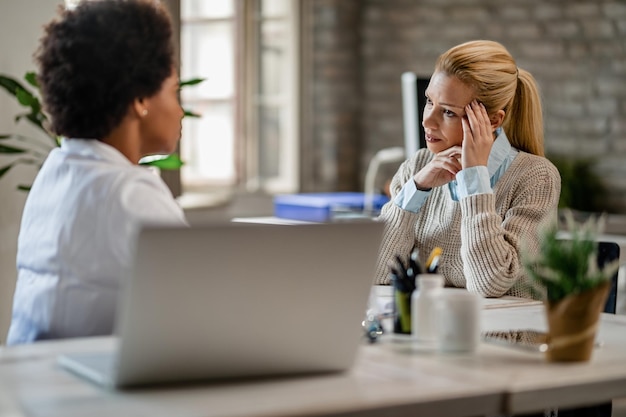 Medio volwassen vrouw die zich zorgen maakt tijdens een gesprek met een Afro-Amerikaanse arts tijdens een medische afspraak