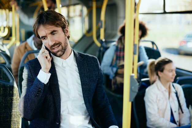 Medio volwassen zakenman die aan de telefoon praat terwijl hij met de bus naar zijn werk reist