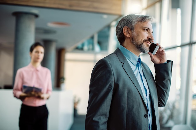 Medio volwassen zakenman die op mobiele telefoon praat terwijl hij in een gang staat