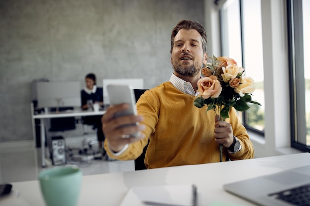 Gratis foto medio volwassen zakenvrouw die een boeket bloemen vasthoudt terwijl ze een videogesprek voert op kantoor