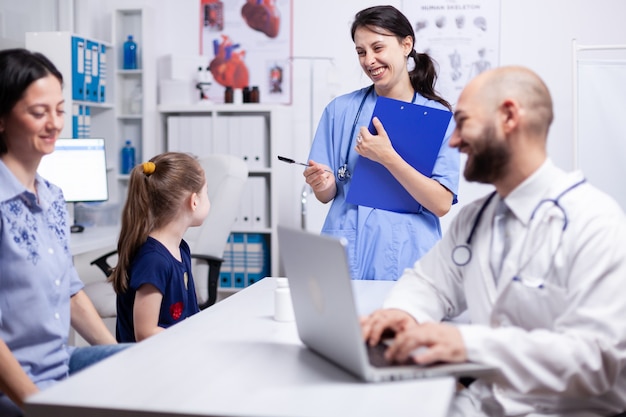 Medisch personeel lacht naar kind tijdens overleg in kantoor aan huis en arts met behulp van laptop. Medisch specialist in de geneeskunde die medische zorg onderzoekt.