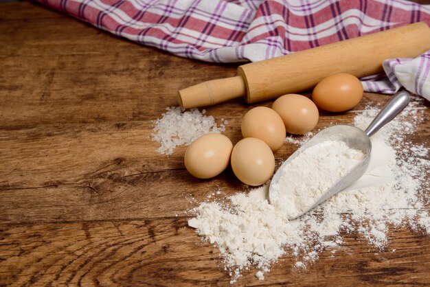 Meel, eieren, zout, handdoek, deegroller op houten tafel klaar om te koken