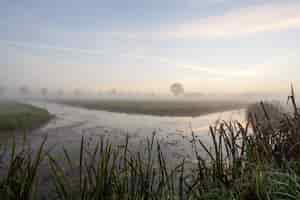 Gratis foto meer in het midden van grasvelden met een mist bij zonsondergang