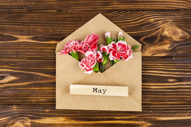 Gratis foto mei-tekst over houten blok op envelop met rode anjerbloemen