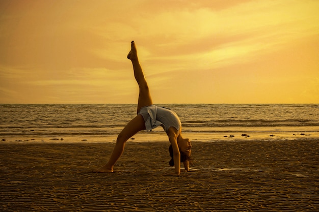 Meisje dat acrobatische bewegingen uitvoert bij het strand in de zonsondergang