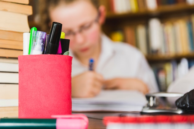 Meisje dat bij bureau met kantoorbehoeften bestudeert