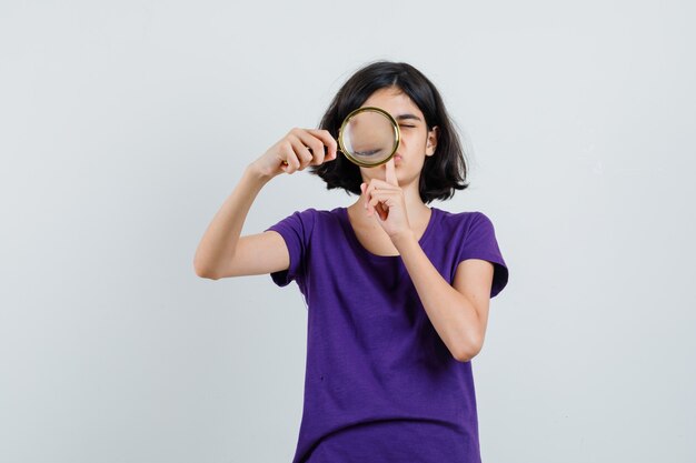 Meisje dat door vergrootglas in t-shirt kijkt