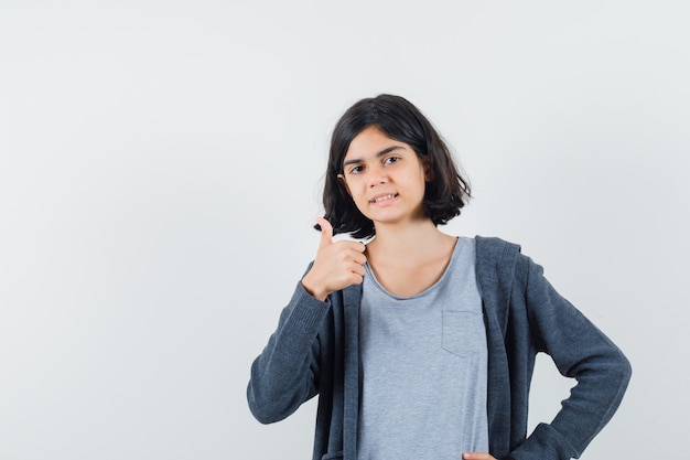 Meisje dat duim in t-shirt, jasje toont en zelfverzekerd kijkt.