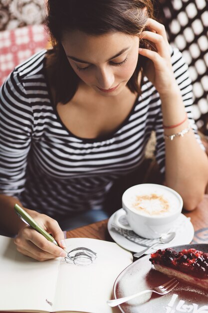 Meisje dat een kop van koffie in het notitieboekje trekt