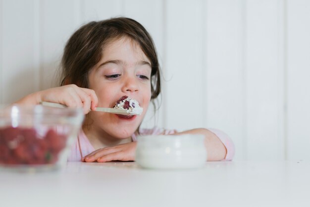 Meisje dat framboos met room eet