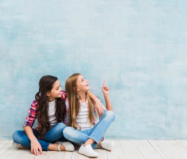 Meisje dat haar glimlachende vriend bekijkt die vinger tegen blauwe achtergrond benadrukt