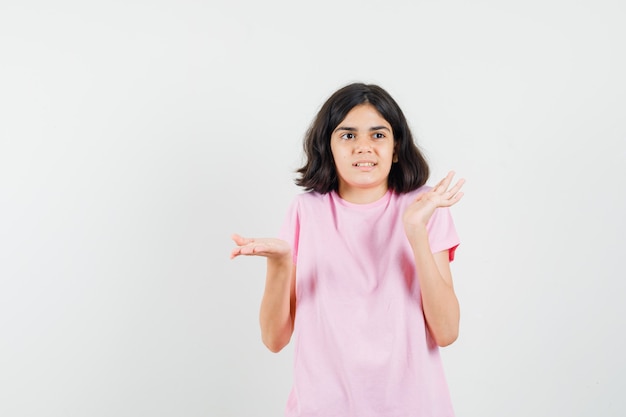 Meisje dat hulpeloos gebaar toont door in roze t-shirt op te halen en verward, vooraanzicht te kijken.