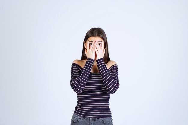 Meisje dat in gestreept overhemd door haar vingers kijkt.