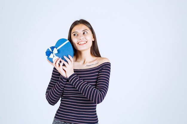 Meisje dat in gestreept overhemd een blauwe hartvormige giftdoos houdt en glimlacht.