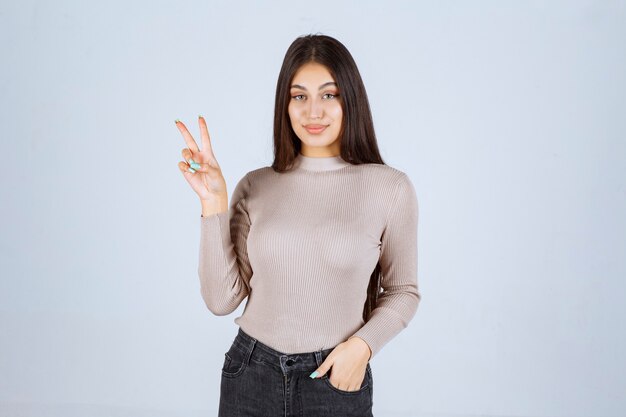 Meisje dat in grijze sweater hand vredesteken doet.