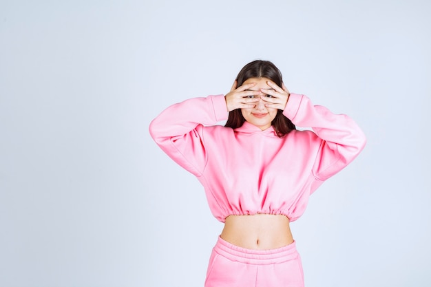 Meisje dat in roze pijamas door haar vingers kijkt