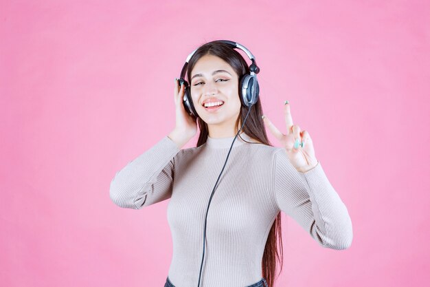 Meisje dat met hoofdtelefoons de muziek luistert en vredesteken toont