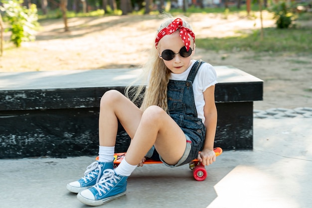 Meisje dat met zonnebril op skateboard zit