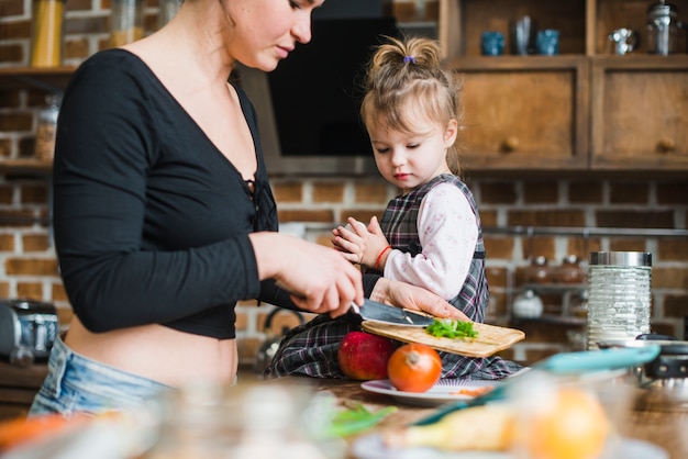 Meisje dat moeder bekijkt die salade maakt