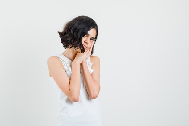 Meisje dat op handpalmen leunt als hoofdkussen in witte blouse en leuk, vooraanzicht kijkt.