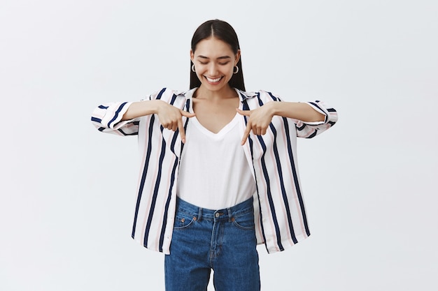 Meisje dat opschept over nieuwe stijlvolle schoenen die ze heeft gekocht. Portret van charmante gelukkig donkerharige vrouw in gestreepte blouse, kijken en naar beneden wijzend met wijsvingers, leren hoe skaten op skeelers