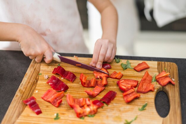 Meisje dat rode groene paprika op hakbord snijdt