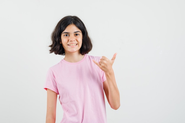 Meisje dat shaka-teken in roze t-shirt maakt en blij, vooraanzicht kijkt.