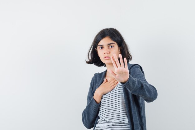 Meisje dat stopgebaar in t-shirt, jasje toont en bang kijkt.