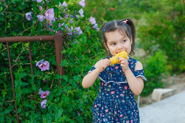 Meisje dat verse maïs eet terwijl hij in de lentekleding in tuin, vooraanzicht staat.