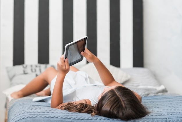 Meisje die op bed liggen die digitale tablet gebruiken