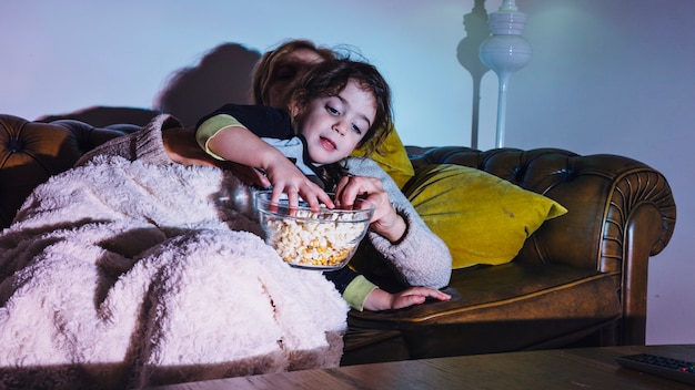 Gratis foto meisje die van avond met moeder genieten die popcorn hebben