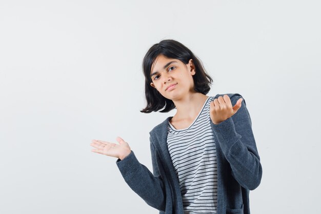 Meisje doet alsof ze iets in t-shirt, jasje laat zien en er zelfverzekerd uitziet.