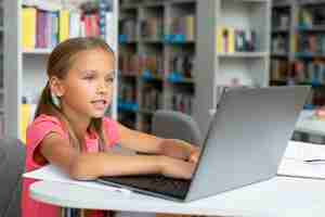 Gratis foto meisje doet haar huiswerk op de laptop in de bibliotheek