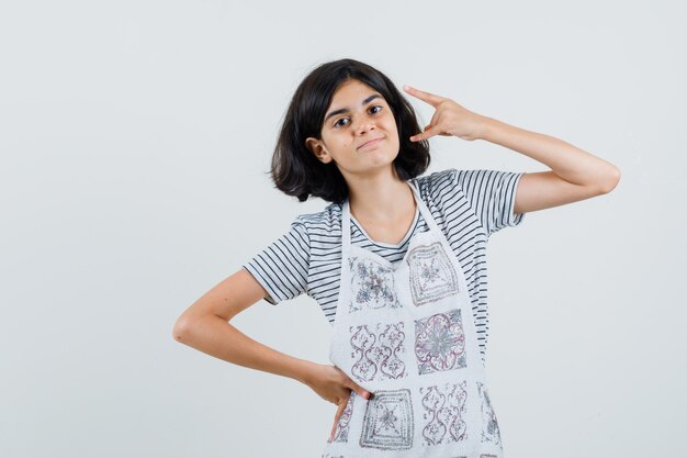 Meisje doet rotssymbool in t-shirt, schort en ziet er zelfverzekerd uit.