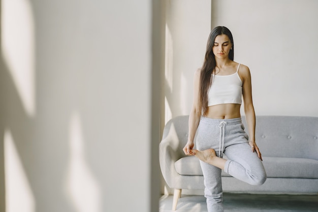 Meisje doet yoga oefeningen thuis in de buurt van sofa en raam in sportkleding
