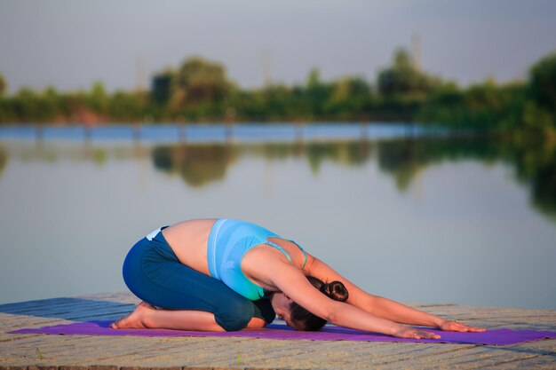 Meisje doet yoga op de oever bij zonsondergang.