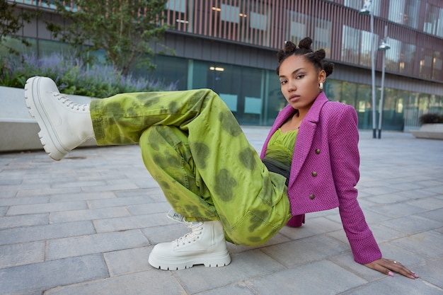 meisje draagt modieuze kleding en witte laarzen heeft lichte make-up poses tegen stedelijke gebouwen poses om fotopraktijken te maken breakdance ziet er serieus uit