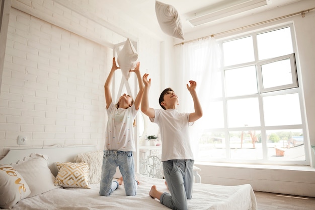 Meisje en jongen die hoofdkussen op bed thuis werpen