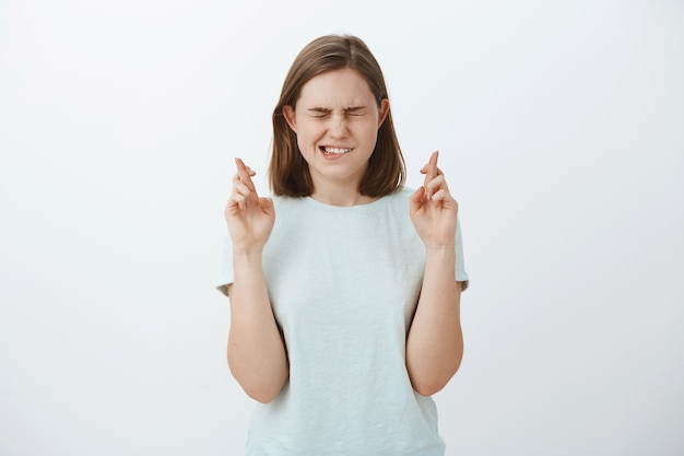 Meisje gelooft dat wonderen kunnen gebeuren als het moeilijk is. Intens hoopvol charmant vrouwtje met schattige flick-ear sluitende ogen en bijtende onderlippen verlangen naar droom die uitkomt vingers kruisen voor geluk