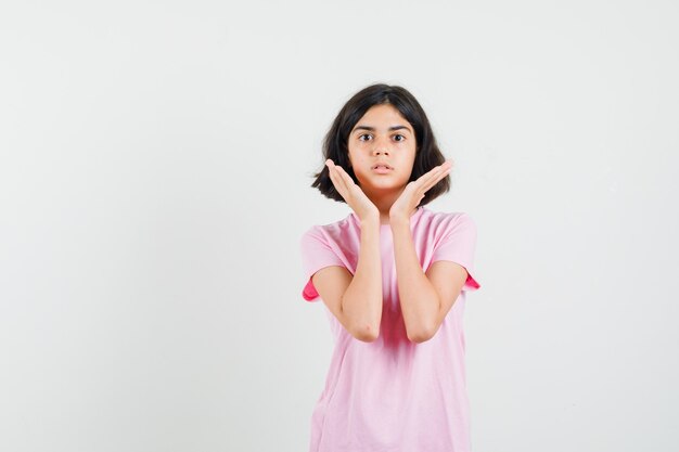 Meisje hand in hand in de buurt van gezicht in roze t-shirt en op zoek verbaasd. vooraanzicht.