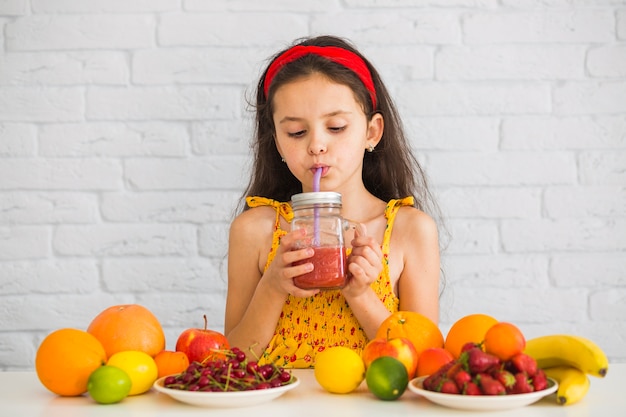 Gratis foto meisje het drinken aardbei smoothies met kleurrijke vruchten