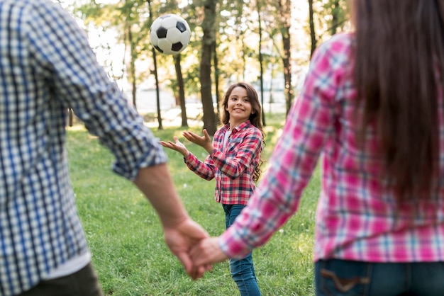 Gratis foto meisje het spelen met voetbalbal voor ouder die elkaar houden dient park in