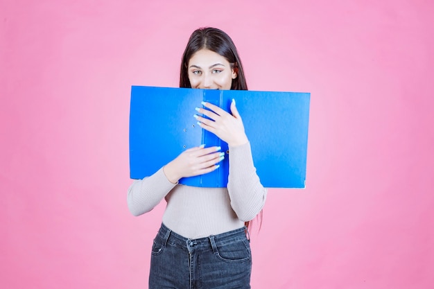 Meisje houdt een blauwe projectmap vast en verbergt haar gezicht erachter