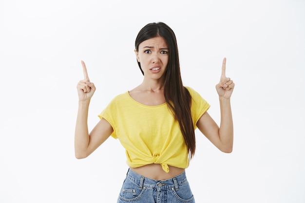 Meisje houdt niet van wat te zien. Ontevreden, onhandig en niet onder de indruk goed uitziende vrouw in geel t-shirt handen omhoog