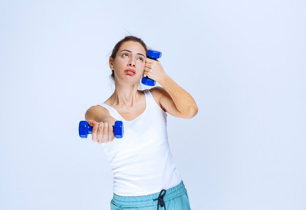 Meisje houdt twee blauwe dumbbells van één kilogram vast en traint ermee.