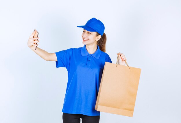 Meisje in blauw uniform met een kartonnen boodschappentas en praten met de telefoon.